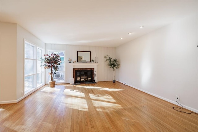 unfurnished living room featuring a fireplace with flush hearth, baseboards, and light wood finished floors