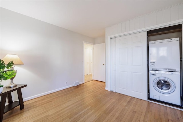 laundry area with hardwood / wood-style floors, baseboards, visible vents, laundry area, and stacked washer and clothes dryer