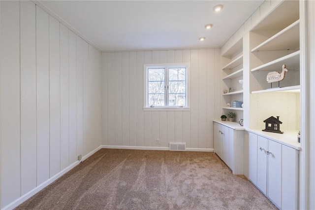 spare room featuring built in features, light colored carpet, visible vents, and baseboards