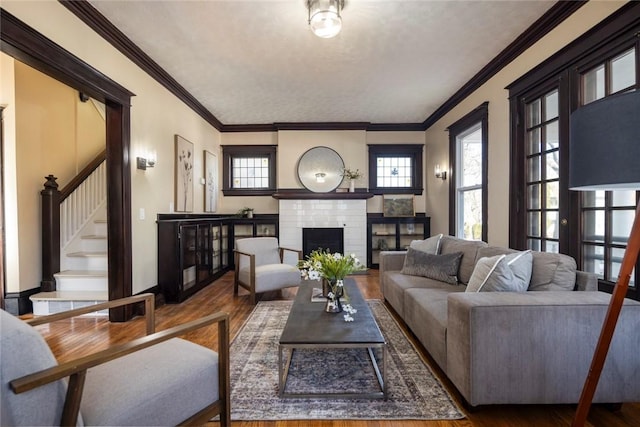 living room featuring ornamental molding, a brick fireplace, stairs, and wood finished floors