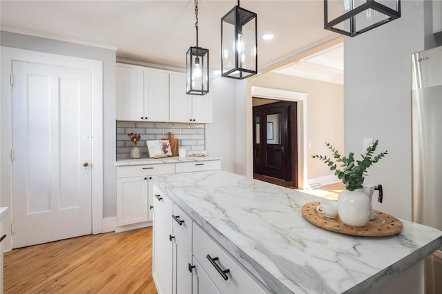 kitchen featuring light wood finished floors, backsplash, light stone countertops, hanging light fixtures, and white cabinets