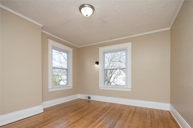 empty room featuring crown molding, a textured ceiling, light wood-type flooring, and baseboards