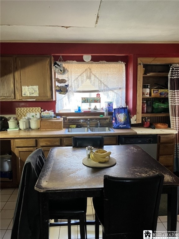 kitchen featuring stainless steel dishwasher, light tile patterned floors, brown cabinetry, and a sink