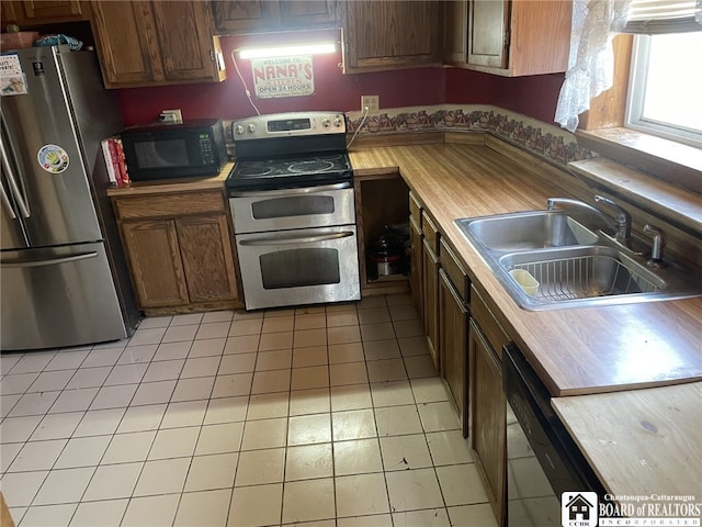 kitchen with wooden counters, light tile patterned floors, brown cabinetry, black appliances, and a sink