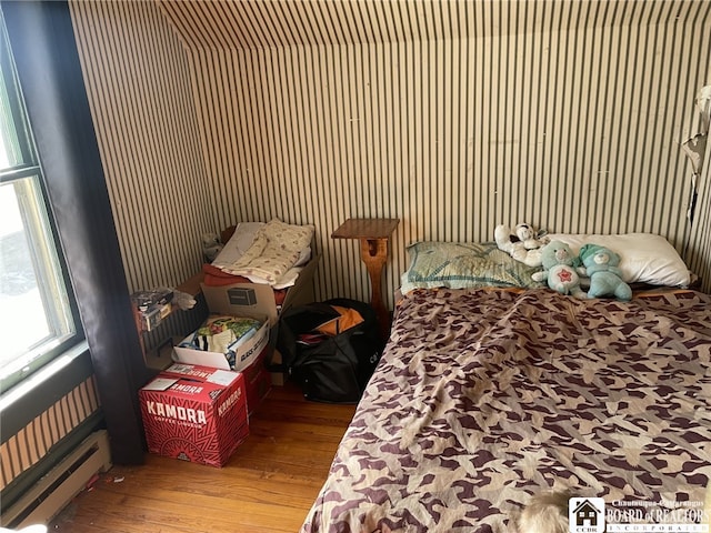 bedroom with a baseboard heating unit and wood finished floors
