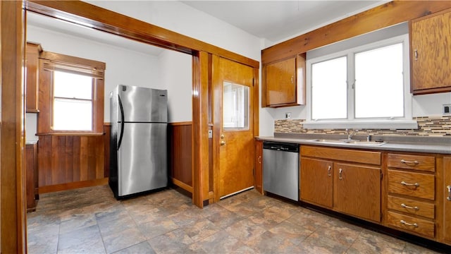 kitchen featuring brown cabinets, a sink, stainless steel appliances, wood walls, and wainscoting