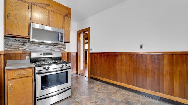 kitchen with a wainscoted wall, stainless steel appliances, light countertops, wood walls, and tasteful backsplash