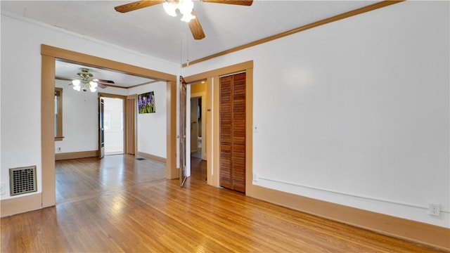 empty room with baseboards, wood finished floors, visible vents, and ornamental molding