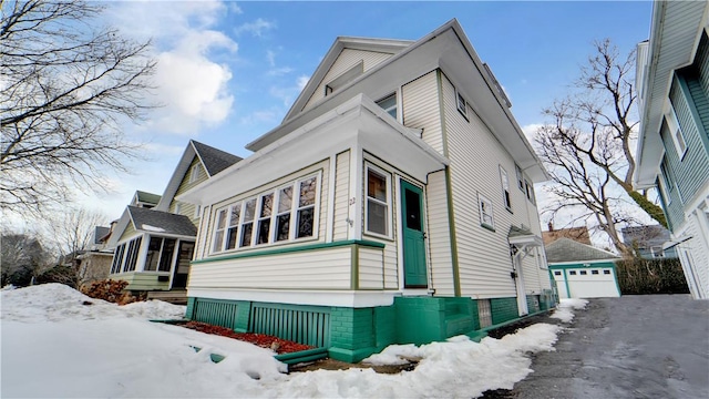 view of snowy exterior with an outbuilding, entry steps, a detached garage, and a sunroom