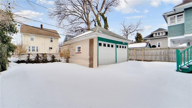 snow covered garage featuring a detached garage and fence