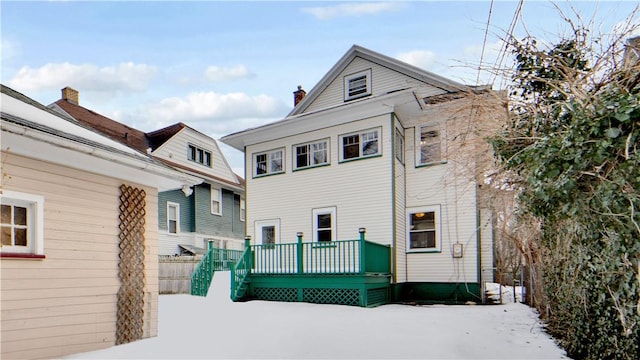 snow covered house with a wooden deck and a chimney