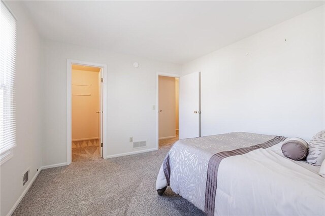 carpeted bedroom with visible vents, a walk in closet, and baseboards