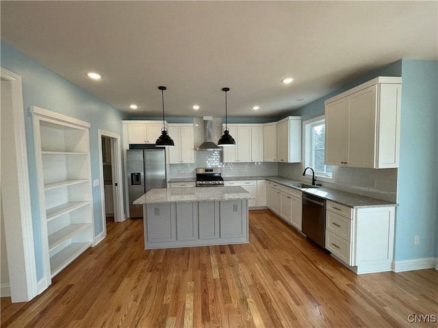 kitchen with a sink, white cabinets, light wood-style floors, appliances with stainless steel finishes, and wall chimney range hood