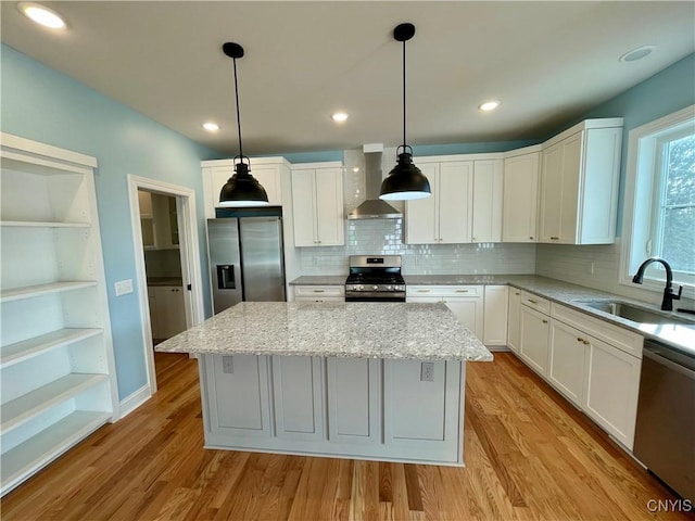kitchen featuring a kitchen island, wall chimney range hood, light wood-style flooring, appliances with stainless steel finishes, and a sink
