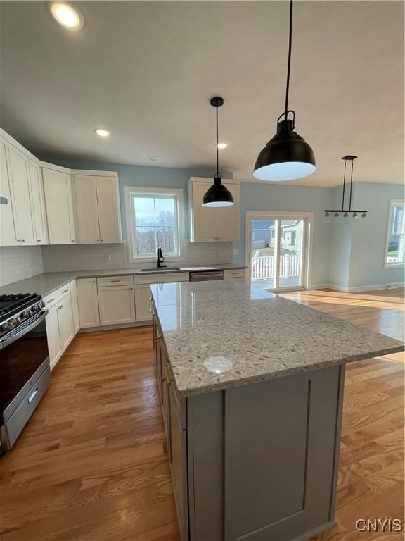 kitchen with light stone counters, light wood finished floors, decorative backsplash, appliances with stainless steel finishes, and white cabinetry