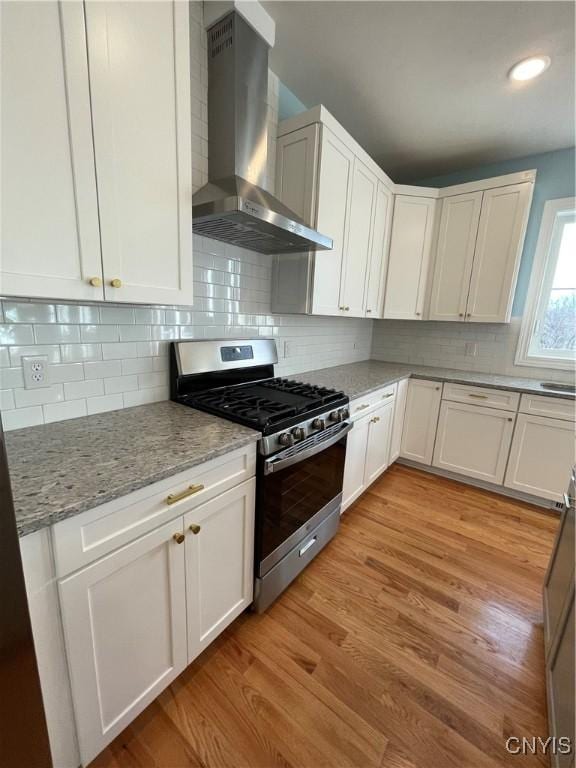 kitchen with gas stove, light wood finished floors, white cabinetry, and wall chimney range hood