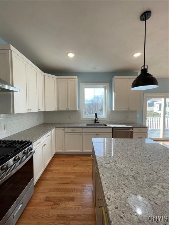 kitchen featuring backsplash, light stone countertops, light wood-style flooring, appliances with stainless steel finishes, and a sink