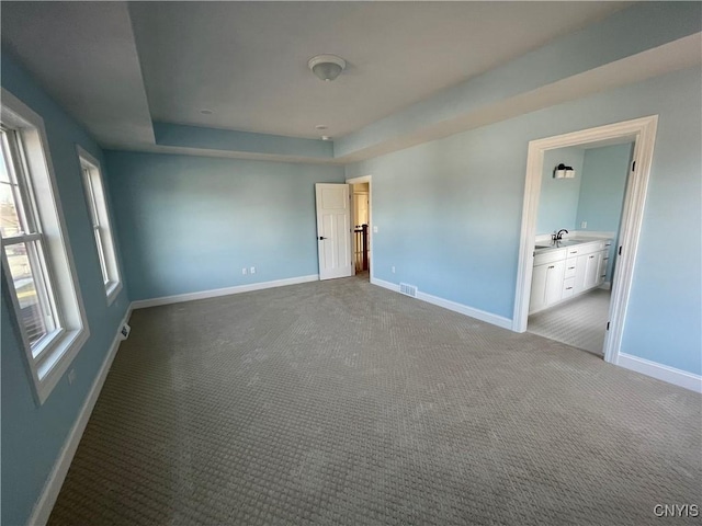 unfurnished bedroom featuring visible vents, baseboards, carpet floors, a raised ceiling, and a sink