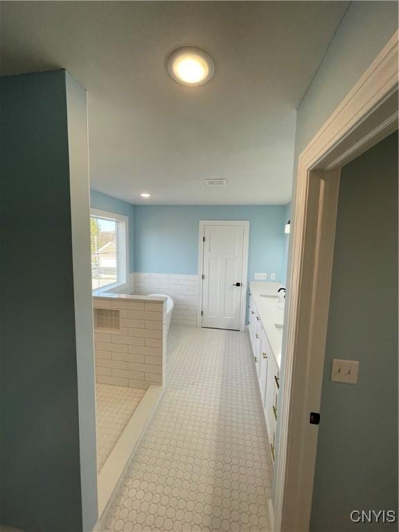 bathroom featuring double vanity, a wainscoted wall, a soaking tub, and tile walls