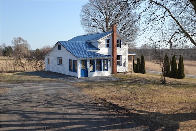 view of front of home with a standing seam roof, a chimney, driveway, and metal roof