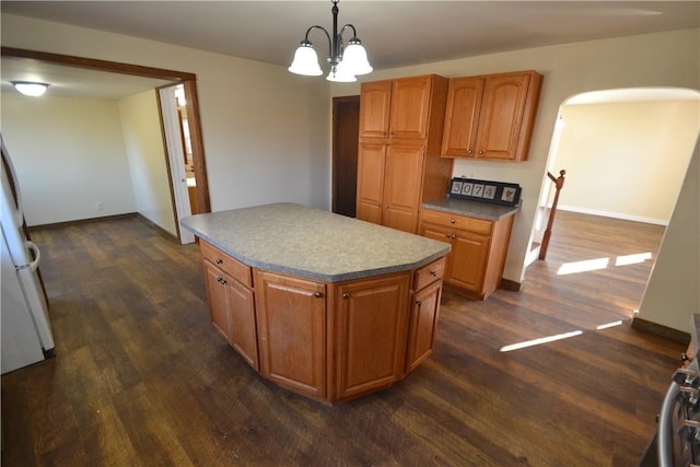 kitchen with arched walkways, brown cabinetry, a kitchen island, and dark wood-type flooring