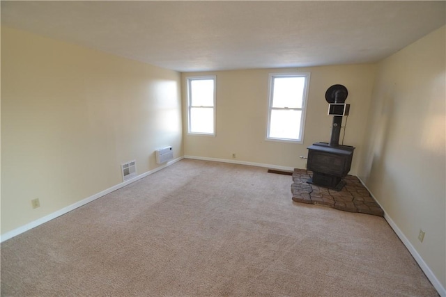 unfurnished living room with visible vents, baseboards, an AC wall unit, carpet flooring, and a wood stove