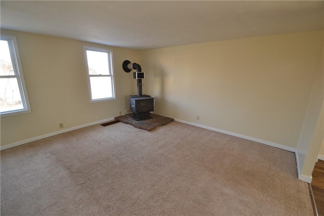 unfurnished living room with carpet flooring, visible vents, a wood stove, and baseboards