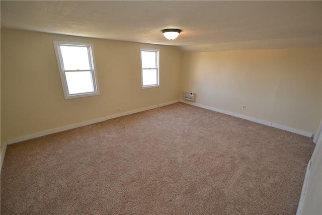 carpeted empty room with a wall unit AC, baseboards, and vaulted ceiling