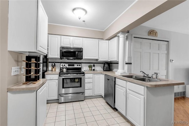 kitchen featuring a peninsula, decorative columns, a sink, stainless steel appliances, and white cabinets