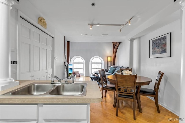 kitchen with light wood-style flooring, a sink, open floor plan, light countertops, and ornate columns