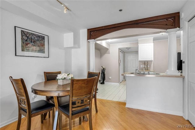 dining area featuring arched walkways, baseboards, light wood-type flooring, and ornate columns