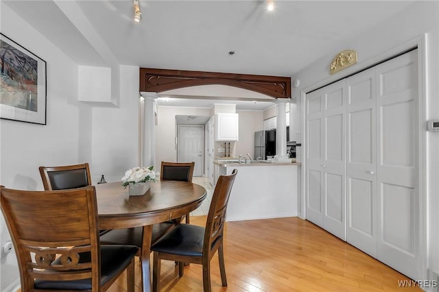 dining space with light wood finished floors, arched walkways, and decorative columns