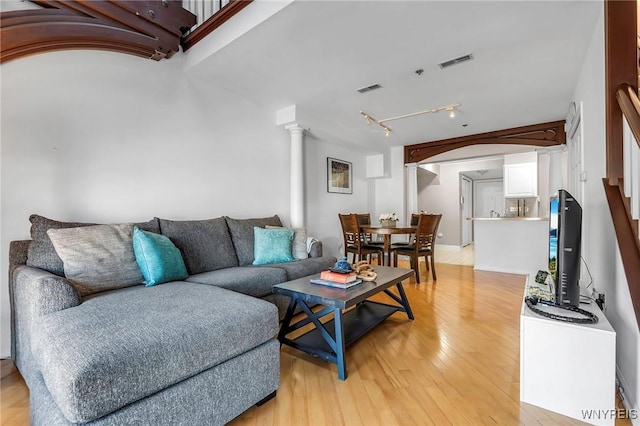 living room featuring visible vents, light wood-style flooring, rail lighting, and ornate columns