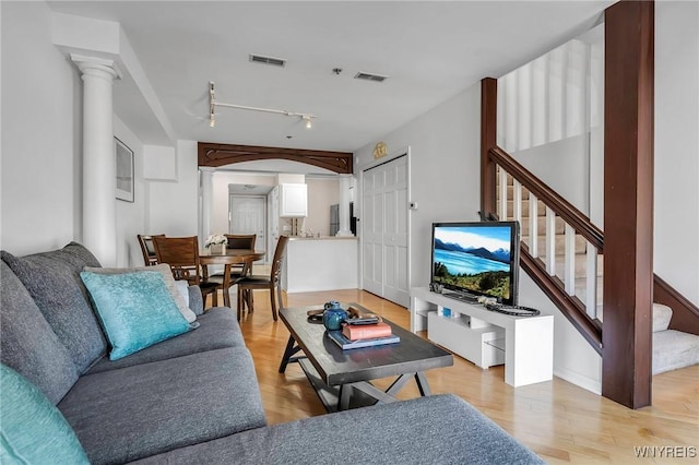 living room featuring ornate columns, stairway, light wood-style floors, and visible vents