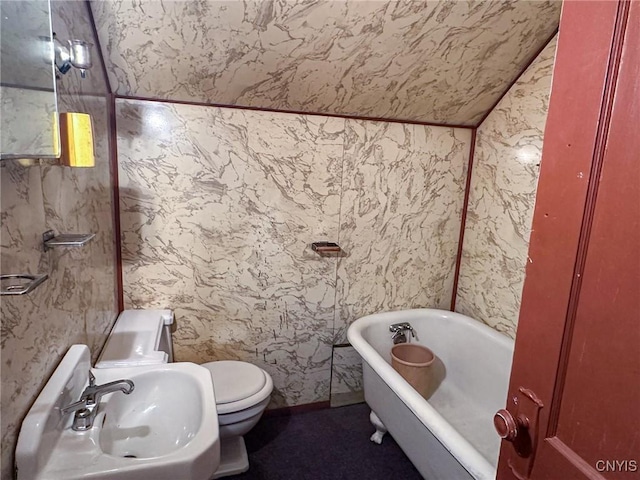 full bath featuring lofted ceiling, a freestanding tub, toilet, and a sink