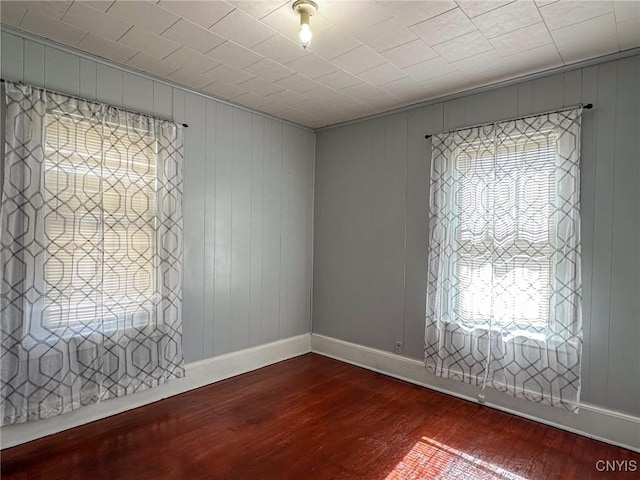 unfurnished room featuring dark wood-style floors, a healthy amount of sunlight, and baseboards