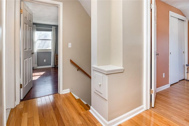 hall with an upstairs landing, baseboards, and light wood finished floors