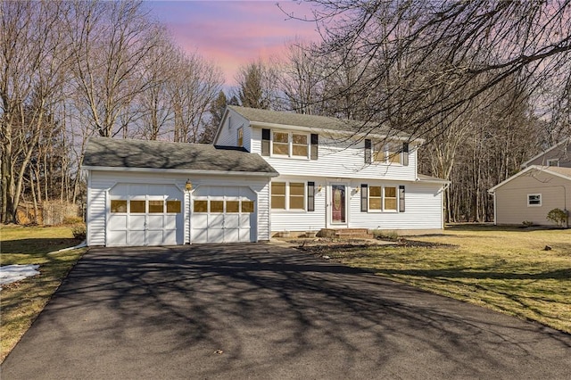 colonial inspired home with aphalt driveway, a lawn, and an attached garage