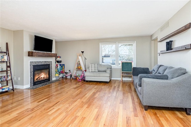 living area with visible vents, baseboards, wood finished floors, and a tiled fireplace