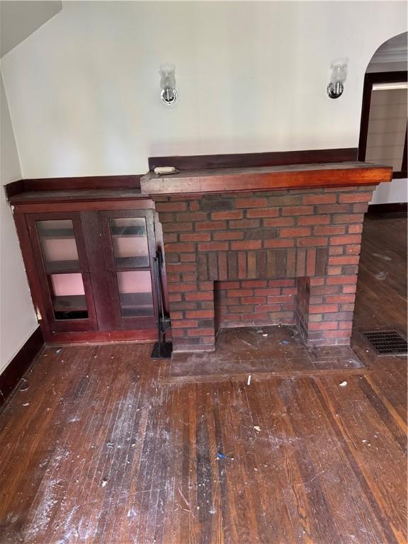 interior details featuring arched walkways, a brick fireplace, baseboards, and wood finished floors