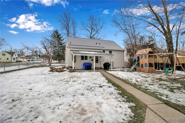 snow covered back of property with a playground, fence, a residential view, and metal roof