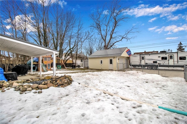 snowy yard featuring an outbuilding, a playground, a garage, and fence