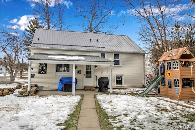 snow covered house featuring a playground and metal roof