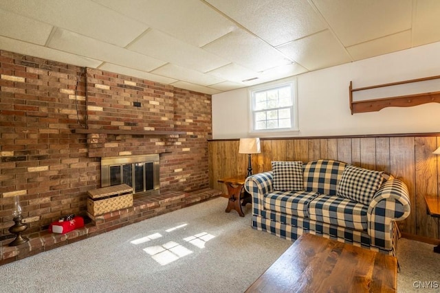 living room with carpet flooring, a brick fireplace, wood walls, and wainscoting