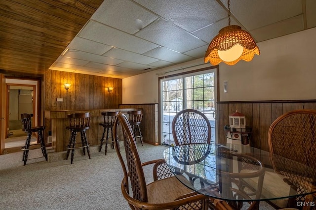 carpeted dining room with a wainscoted wall and wooden walls