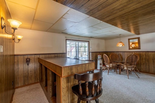 carpeted dining space featuring wooden walls and wainscoting