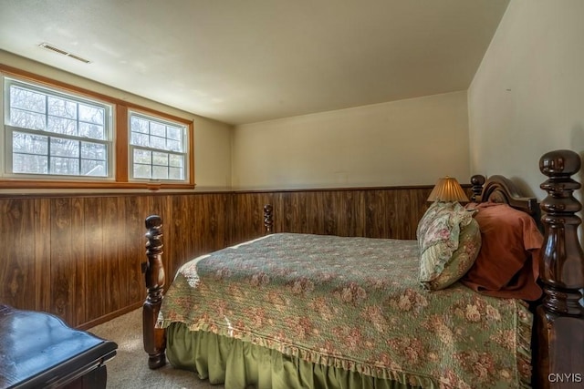 carpeted bedroom featuring wooden walls, a wainscoted wall, and visible vents