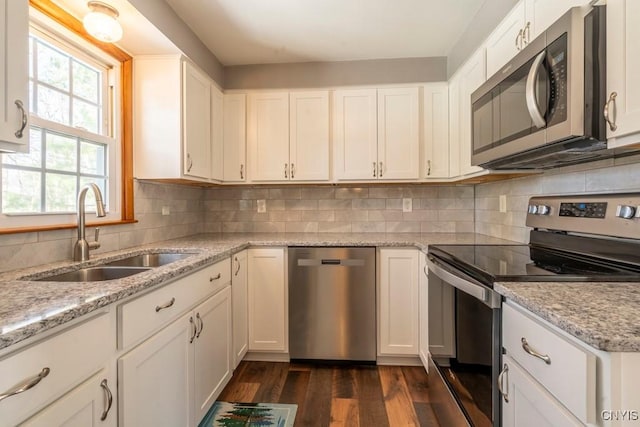 kitchen with dark wood finished floors, decorative backsplash, appliances with stainless steel finishes, white cabinets, and a sink