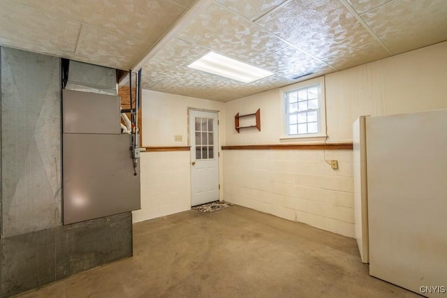 basement with heating unit, concrete block wall, and freestanding refrigerator