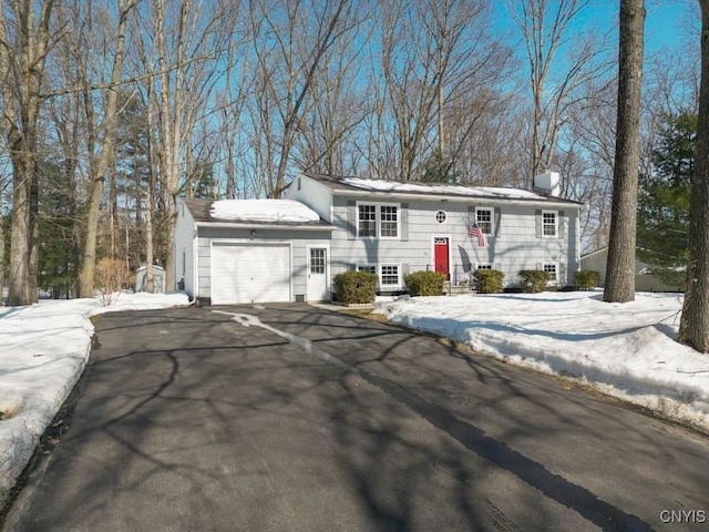 bi-level home featuring a garage, a chimney, driveway, and entry steps